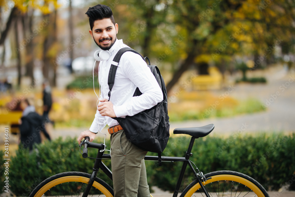 Casual handsome indian businessman pushing bike and carry handsbag going to work by bicycle