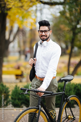 Indian stylish bearded student man with backpack with bicycle walking on street