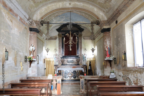An old shabby countryside single nave Catholic church with some benches  statues and moldy paintings in the rural town of Camery  in Piedmont  Italy