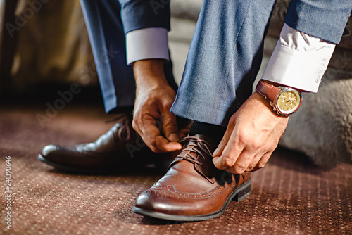 An elegant man puts on black, leather, formal shoes.