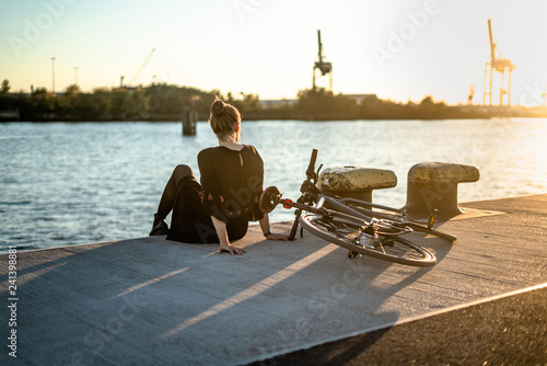 Young woman with her bicycle in harbour while sunset