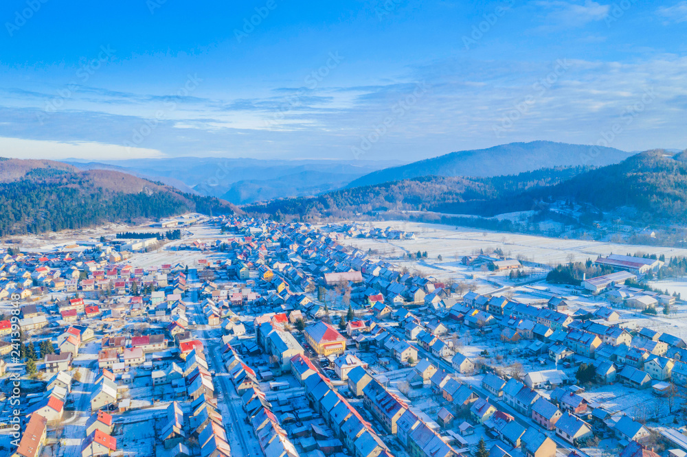 Fototapeta premium Croatia, Delnice, Gorski kotar, panoramic view of town center from drone in winter, mountain landscape in background, houses covered with snow 