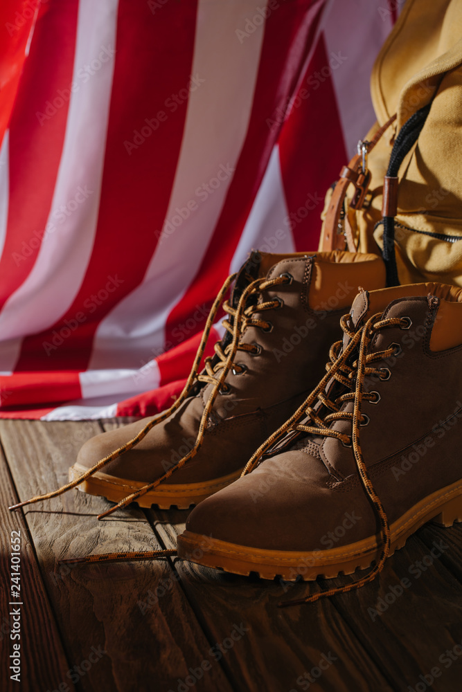 close-up view of trekking boots, backpack and american flag on wooden surface close-up view of trekking boots, backpack and american flag on wooden surface