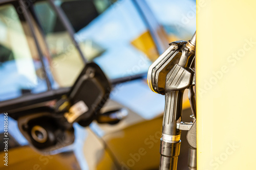 Fuel nozzle at a gas station with fuel tank cap on a car