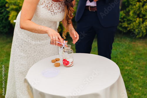 the bride in a beautiful wedding dress pours sand into a unity vase and the groom waits for her turn
