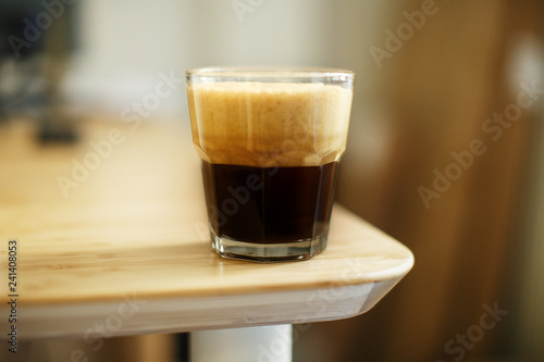 A glass of iced espresso lying on a wooden table corner