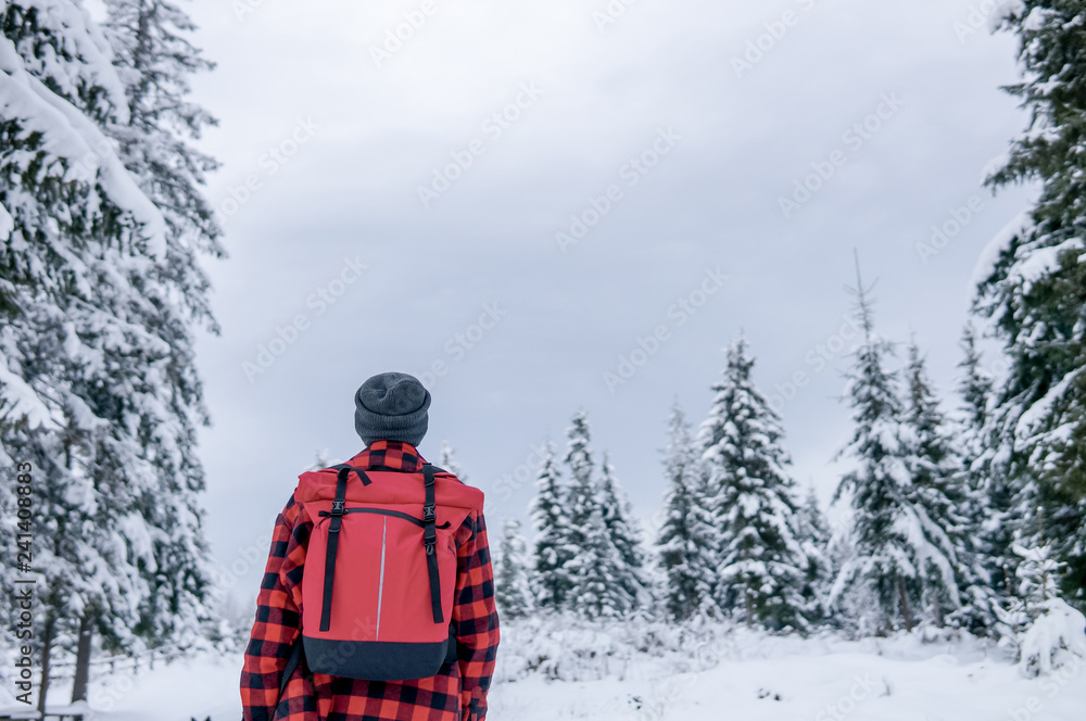 Traveler with a backpack in a warm jacket looks at the winter forest