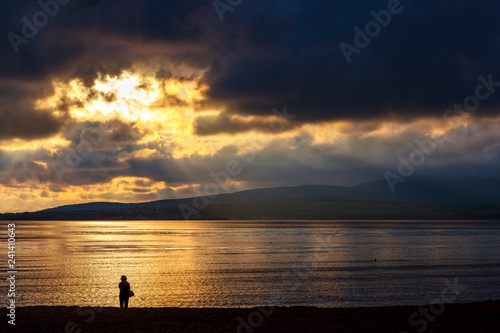 A lone figure in the sunset on the beach. Dramatic sunset, clouds, reflections in the sea, loneliness, thoughtfulness, reflections
