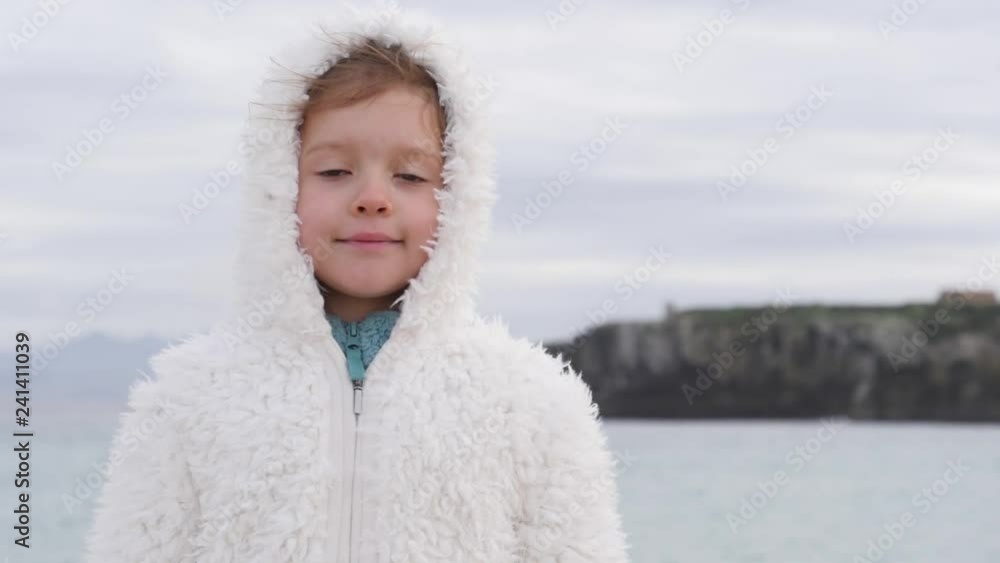 Cute child girl in white coat portrait on the beach in winter Spain coast slow motion Cute child girl in white coat portrait on the beach in winter Spain coast slow motion
