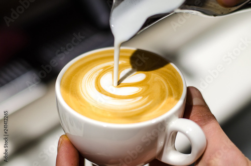 Holding espresso cup and pouring milk to make latte art shapes