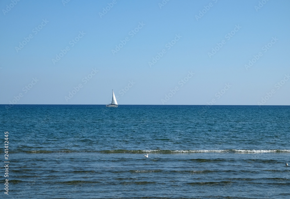 Landscape with yacht with high white sails floats into the calm open sea against clear skyline on bright suppy day