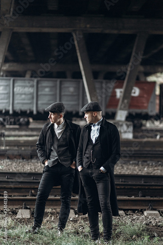 stylish gangsters men, posing on background of railway. england in 1920s theme. fashionable brutal confident group. atmospheric  moments. space for text