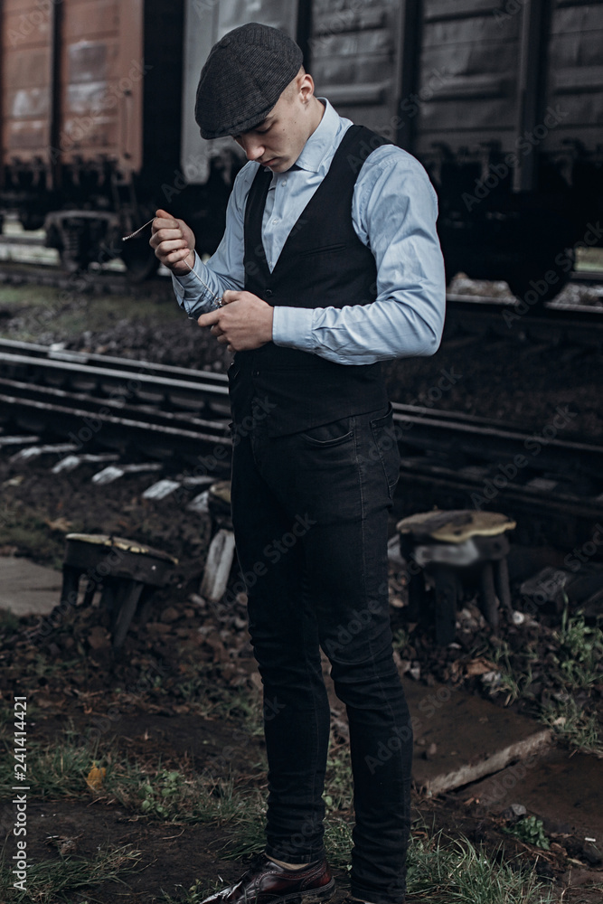 stylish man in retro look smiling posing on background of railway. england in 1920s theme. fashionable brutal confident gangster. atmospheric moments stylish man in retro look smiling posing on background of railway. england in 1920s theme. fashionable brutal confident gangster. atmospheric moments