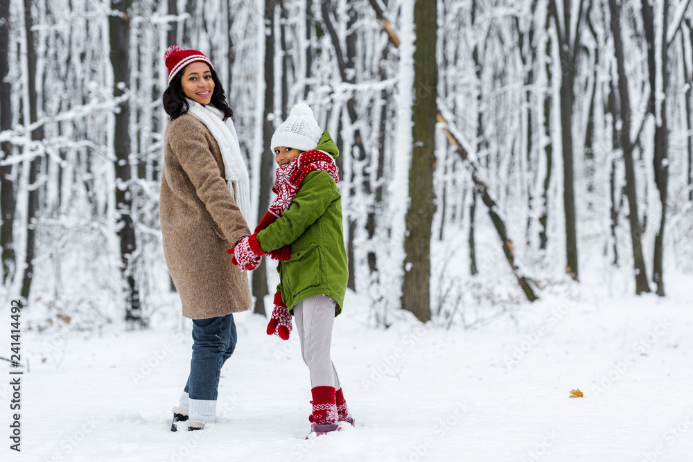 african american mother and daughter, smiling, holding hands and looking at camera in winter park african american mother and daughter, smiling, holding hands and looking at camera in winter park