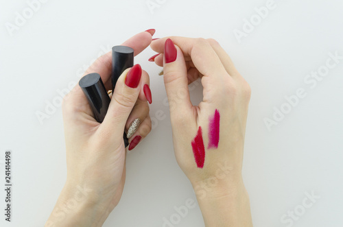 Testing makeup product a swatch of the red lipstick on woman hand with beautyful manucure red nails.Top view.