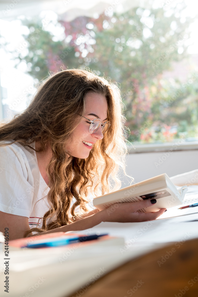 Obraz premium Beautiful young woman reading a book while lying on her bed
