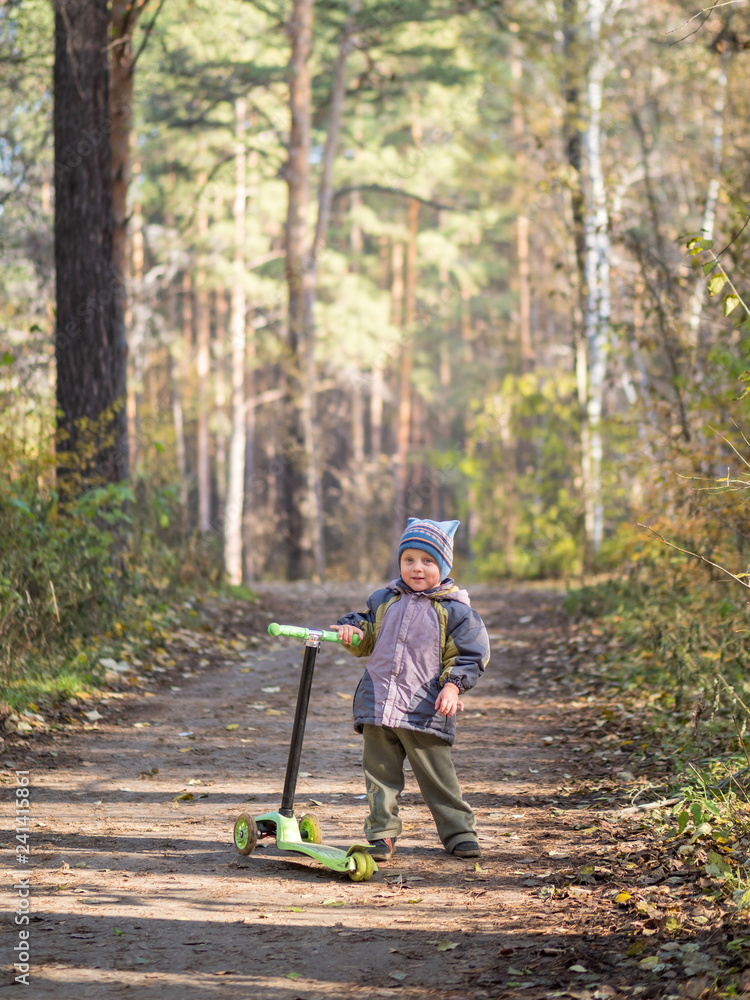 A little boy stands with a scooter in the Park