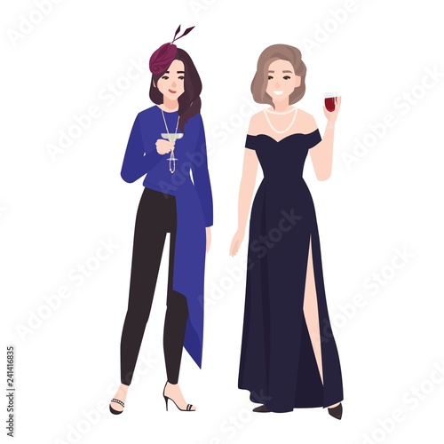 Pair of girls in stylish evening outfits standing together and drinking cockt...