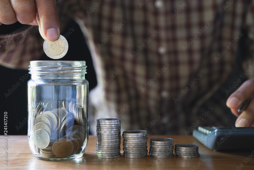 Business man putting coin in glass bottle saving bank and account for his money all in finance accounting concept. Business man putting coin in glass bottle saving bank and account for his money all in finance accounting concept.