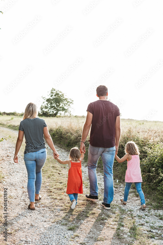 Rear view of family with two daughters walking hand in hand on a field path Rear view of family with two daughters walking hand in hand on a field path
