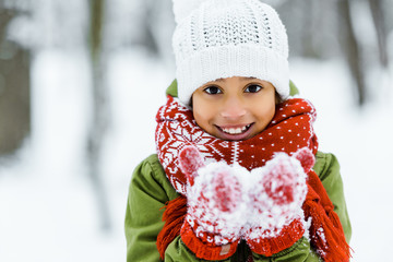 cute african american child showing white snow an smiling at camera in winter forest