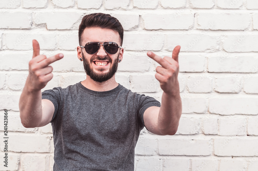Naklejka premium Portrait of a handsome young man standing against a white brick wall. Smile, indecent gestures.