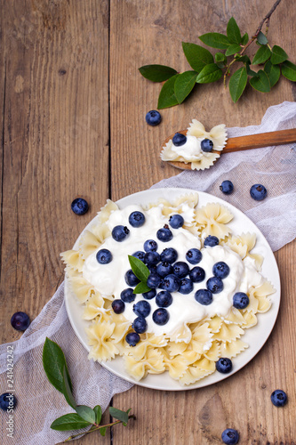 Tasty pasta with fresh organic blueberries and vanilla cream. Sweet dinner on retro wooden table.