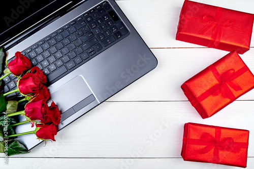 Open laptop computer, bouquet of red roses and gift boxes on white wooden desk in office, copy space. Flat lay, top view. Online shopping, sale. Valentines day, March 8, Womens Day, Mothers day © mirage_studio