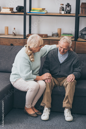 senior woman sitting near retired husband and holding hands in living room