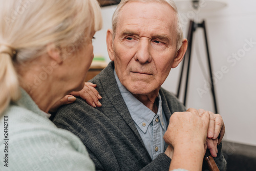 selective focus of sad pensioner looking at retired wife at home