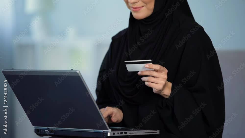 Pretty female in hijab entering credit card number on laptop, shopping online Pretty female in hijab entering credit card number on laptop, shopping online