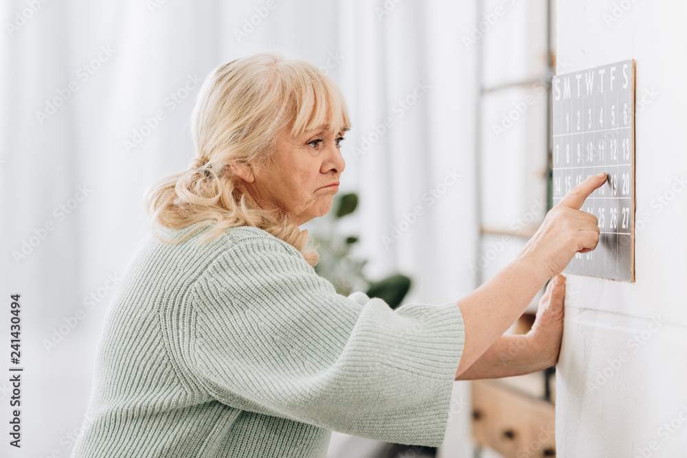 © LIGHTFIELD STUDIOS - upset senior woman touching wall calendar and remembering dates