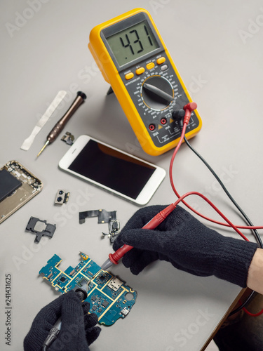 Technician or engineer using digital multimeter to electric current measurement on smartphone logic board for diagnosis broken smartphone 