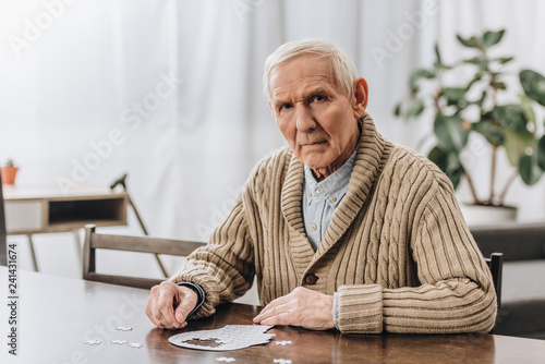sad pensioner with grey hair playing with puzzles at home