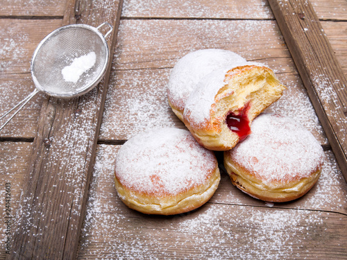 Tradycyjne pączki z cukrem pudrem i nadzieniem na drewnianym tle. Smaczne pączki z dżemem 