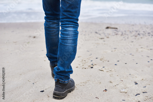 A man Take a walk along the seashore.Men wear shoes and Jeans walk out