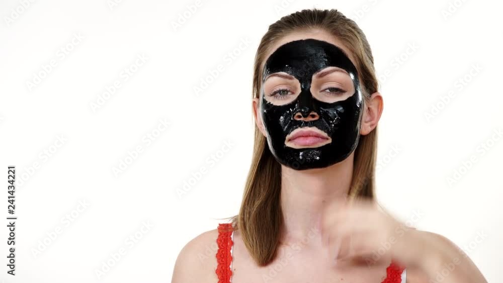 Young woman with carbo detox black peel-off mask on her face, on white. Teen girl taking care of oily skin, cleaning the pores. Beauty treatment. Skincare Young woman with carbo detox black peel-off mask on her face, on white. Teen girl taking care of oily skin, cleaning the pores. Beauty treatment. Skincare