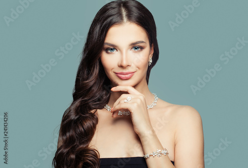 Happy girl with jewelry. Brunette woman with makeup and curly hairstyle and diamond necklace on blue background