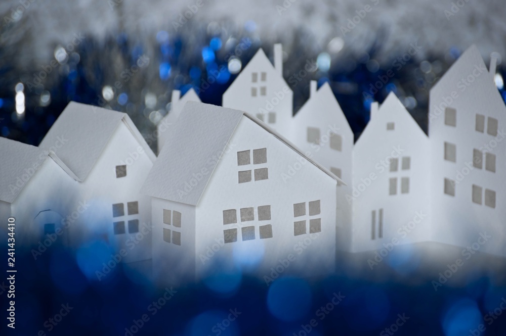 Handmade small white cardboard houses with cut windows on dark blue bokeh foreground and background. Winter decoration. Shallow depth of focus. Handmade small white cardboard houses with cut windows on dark blue bokeh foreground and background. Winter decoration. Shallow depth of focus.