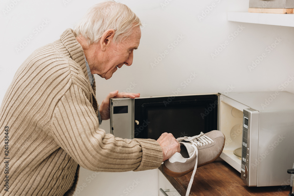 retired man with dementia disease putting shoe in microwave oven Stock