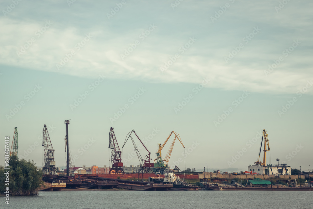 A barge in the river port and working cranes on the city background 