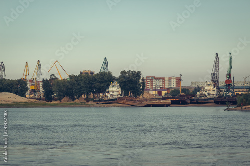 A barge in the river port and working cranes on the city background 