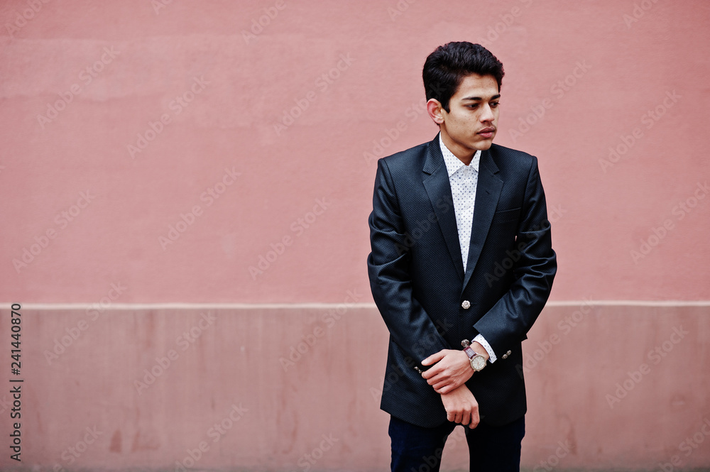 Young indian man on suit posed against pink wall.