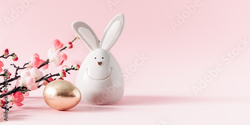 Easter golden eggs, pink flowers and porcelain rabbit on pastel pink background. Easter, spring concept. Copy space, banner