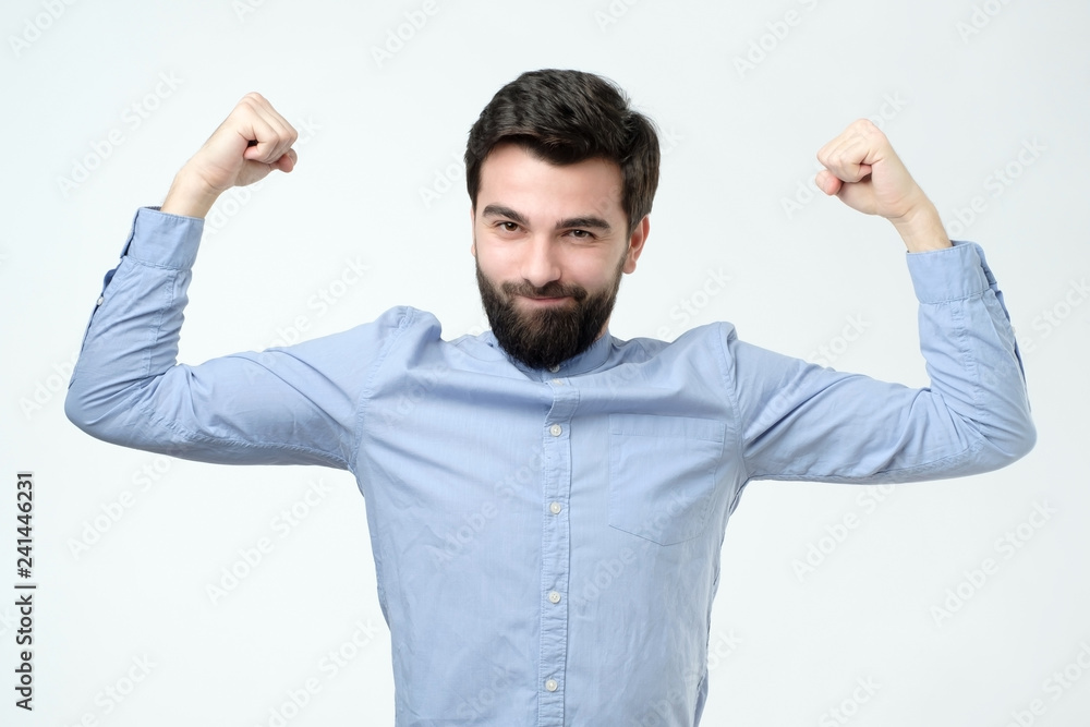 Strong man clenches fists, dressed in casual blue shirt, celebrates his victory Strong man clenches fists, dressed in casual blue shirt, celebrates his victory