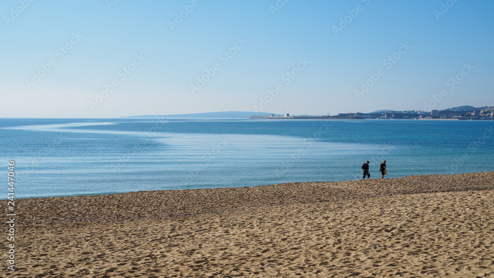 Pareja paseando en invierno por la playa con el mar en calma Pareja paseando en invierno por la playa con el mar en calma