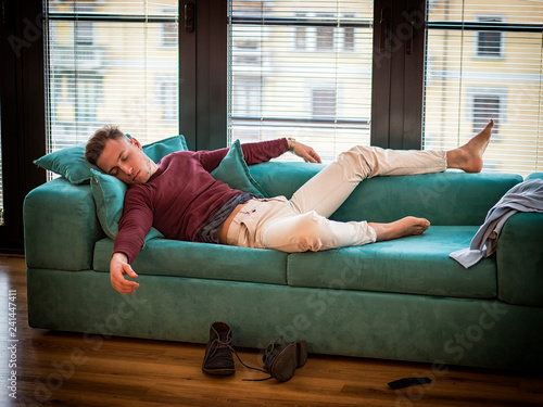 Drunk Young Handsome Man Resting on Couch in the Living Room with Head on the Floor.
