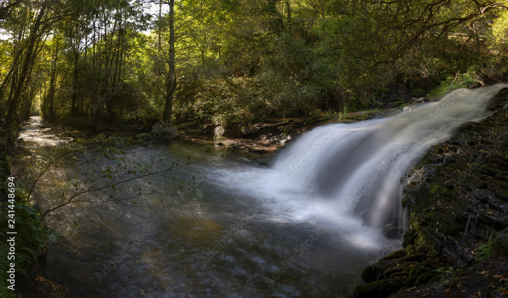 Waterfall and channel of a river between deciduous forests Waterfall and channel of a river between deciduous forests