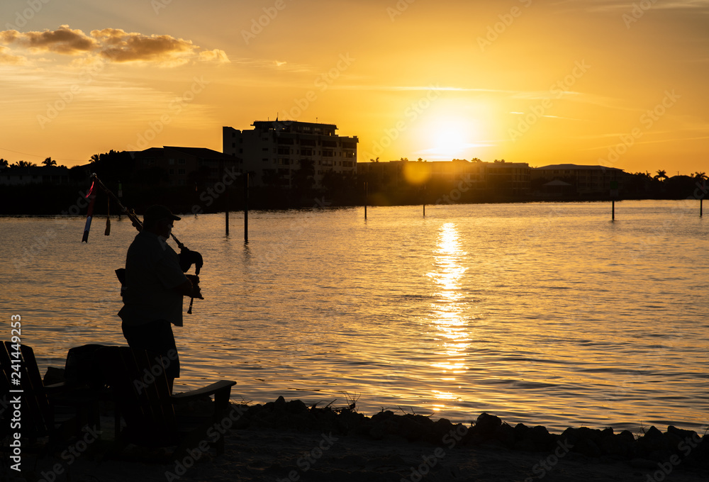 A bagpiper playing, silhouetted against the sunset