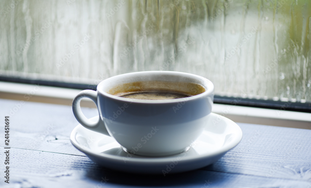 Wet glass window and cup of hot coffee. Autumn cloudy weather better with caffeine drink. Enjoying coffee on rainy day. Fresh brewed coffee in white cup or mug on windowsill. Coffee time on rainy day Wet glass window and cup of hot coffee. Autumn cloudy weather better with caffeine drink. Enjoying coffee on rainy day. Fresh brewed coffee in white cup or mug on windowsill. Coffee time on rainy day